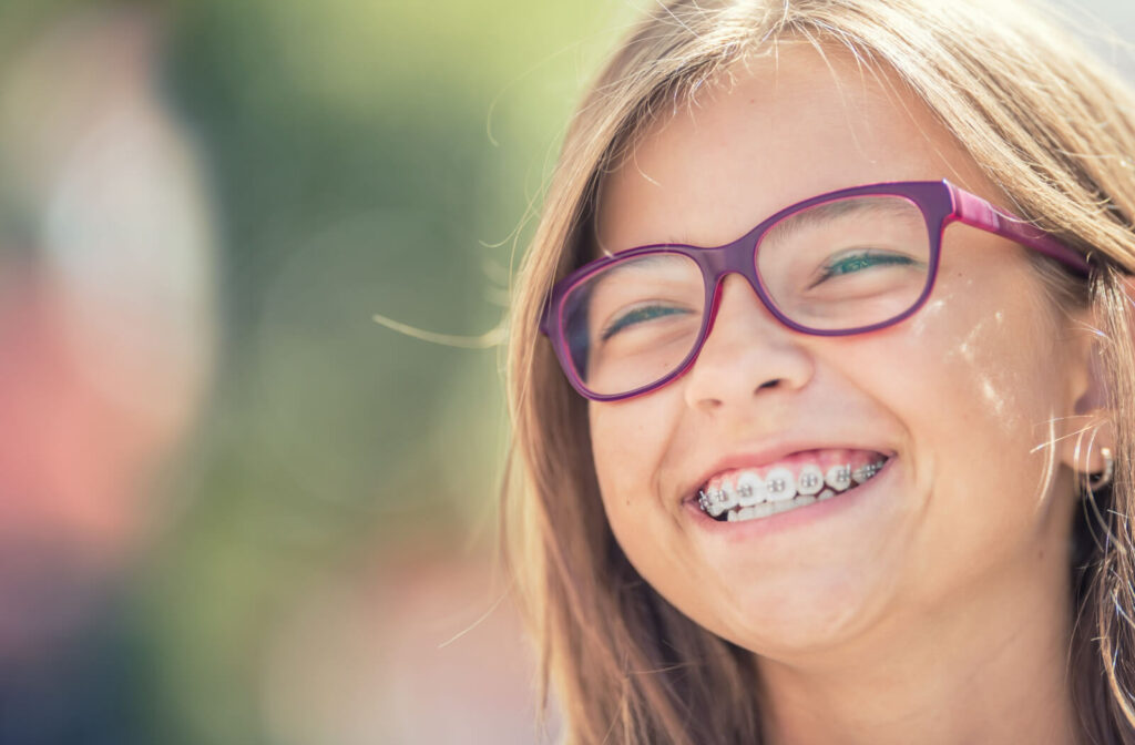 Close-up of a young child, smiling with dental braces and glasses