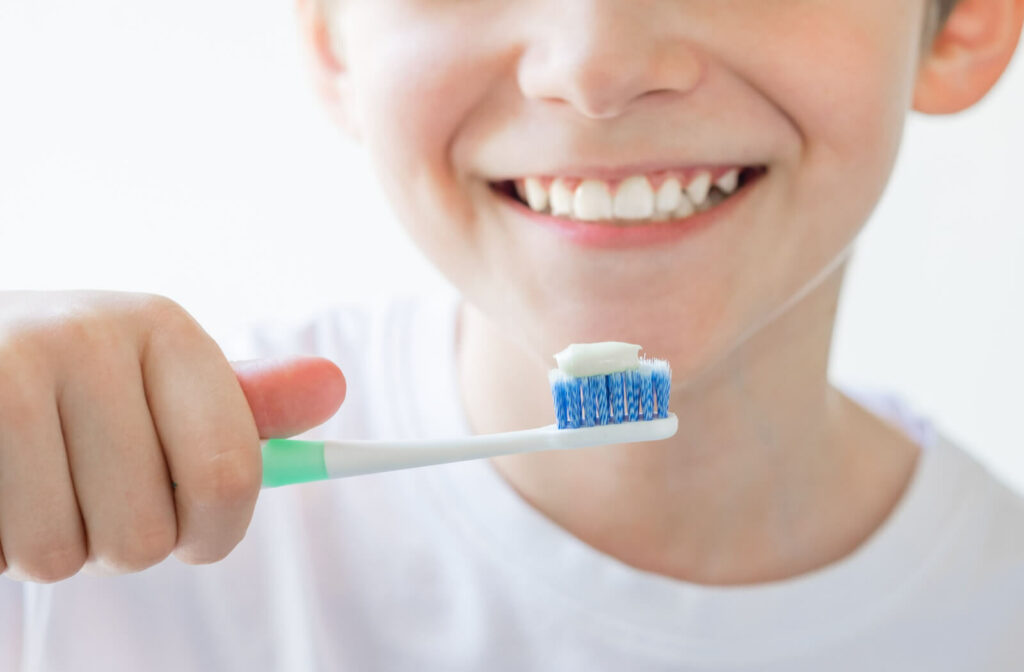 Close-up of young child smiling and holding a toothbrush with toothpaste in his right hand